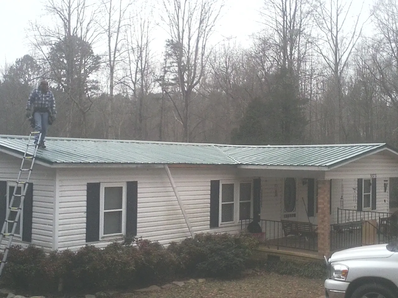 Worker on a ladder beside a new green metal roof on a ranch home in Wauconda
