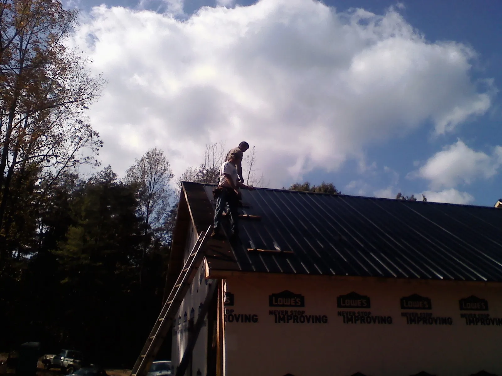 Roofer fastening dark metal panels high against a cloudy sky, from a Roof Inspection job in Wauconda